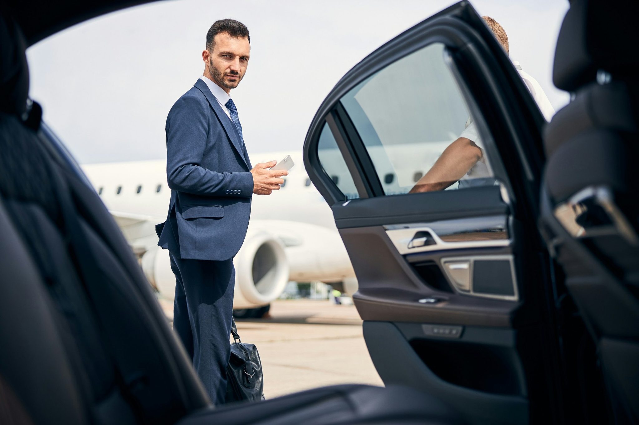 A chauffeur holding the car door open beside a private jet